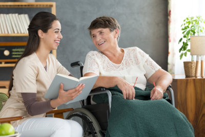 senior woman in wheelchair and caregiver reading book at loud